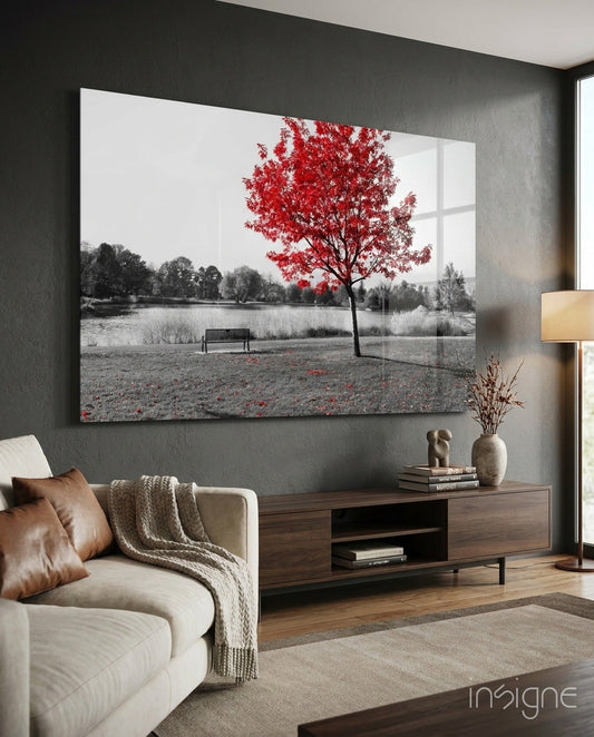 Glass wall art displaying a black and white lakeside scene with a solitary red tree and bench, installed above a wooden media console in a modern living room.
