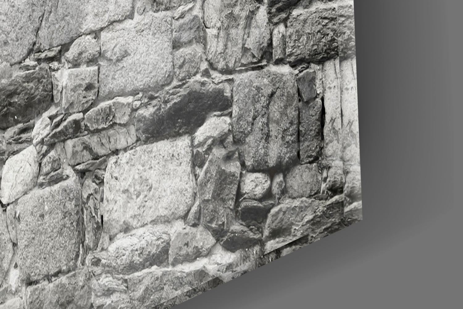 Close-up of weathered stone wall with light gray rectangular blocks stacked in offset rows, showing texture and shadows.