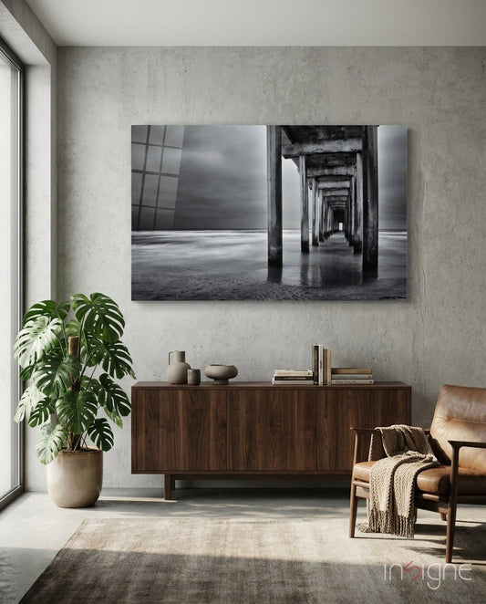Black and white glass wall art depicting a pier's underside with repeating columns receding into distance, displayed above wooden credenza in modern living room.