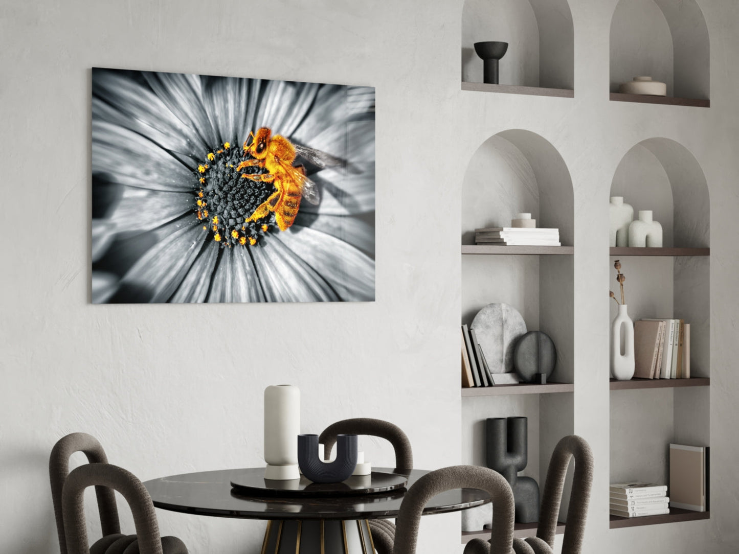 Glass wall art depicting a close-up bee on a white and gray flower with yellow pollen, displayed above a black dining table.