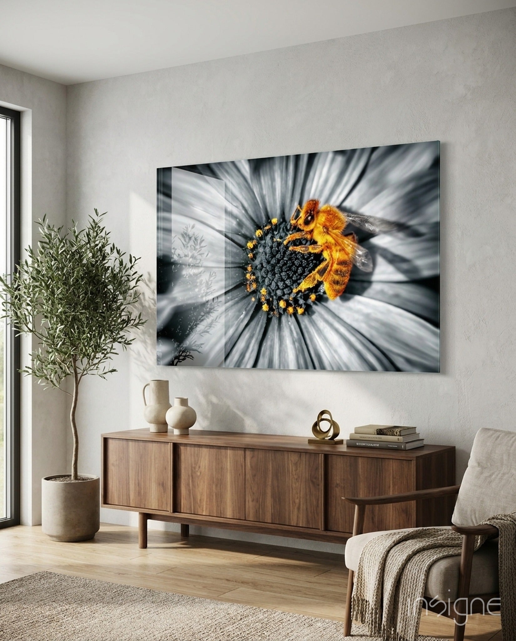 Honey bee glass wall art mounted above wooden credenza in modern living room with plant and chair visible.