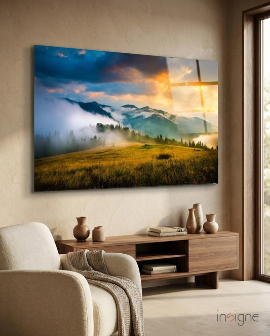 Golden Sunset Meadow Misty Mountains glass wall art hanging above wooden console table in neutral living room with cream chair.