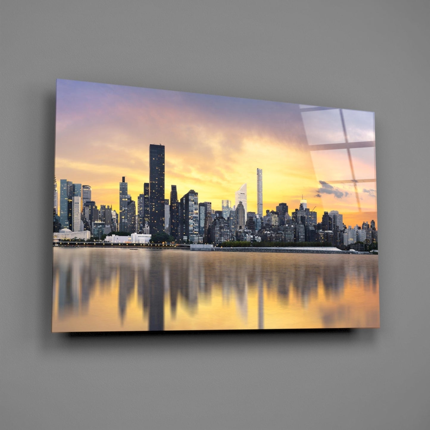 Glass wall art displaying Manhattan skyline at golden sunset with water reflections, mounted on gray wall.