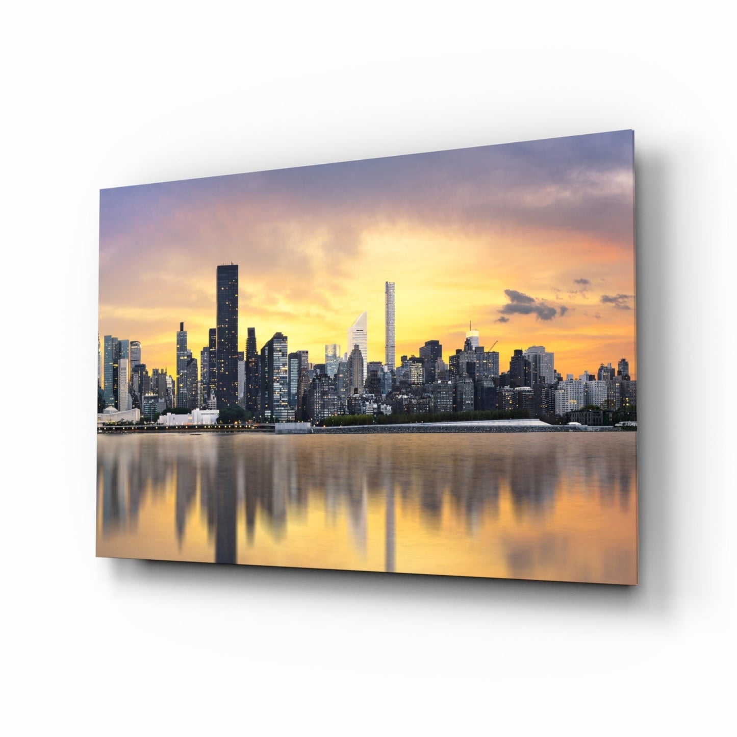 Manhattan skyline at sunset reflected in still water, printed on angled glass panel displaying warm golden and orange sky tones.