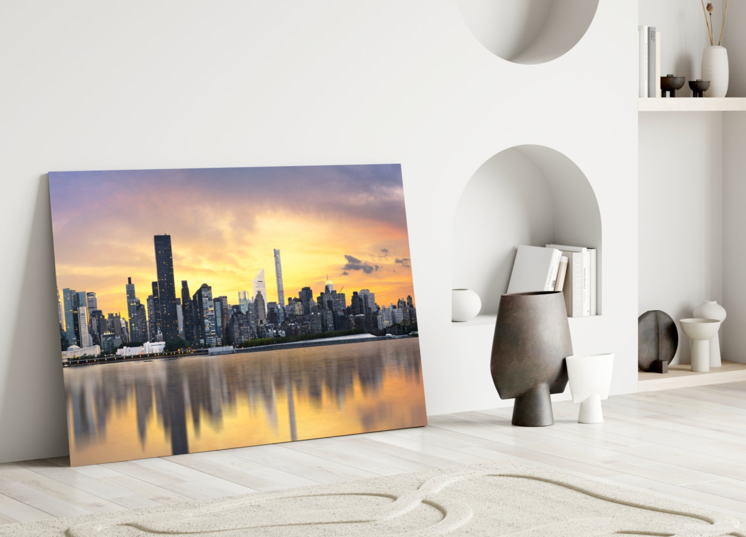Glass wall art leaning against white wall displays golden sunset over Manhattan skyline reflected in water.