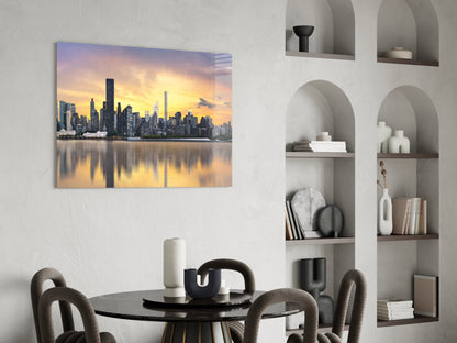 Glass wall art depicting a golden-hour Manhattan skyline with waterfront reflection, displayed above a dining table in a modern interior.
