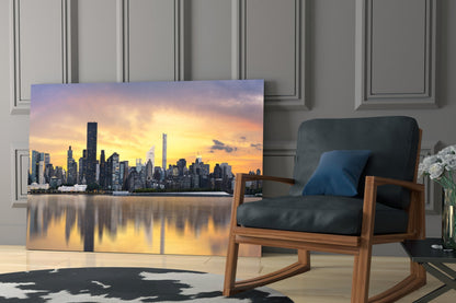 Glass wall art depicting a sunset Manhattan skyline with golden sky reflections displayed in a modern living room beside a wooden chair.