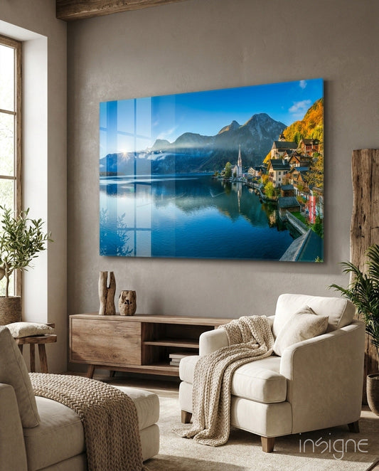 Glass wall art depicting Alpine lakeside village with mountains, reflecting on water, displayed above wooden console in neutral living room.