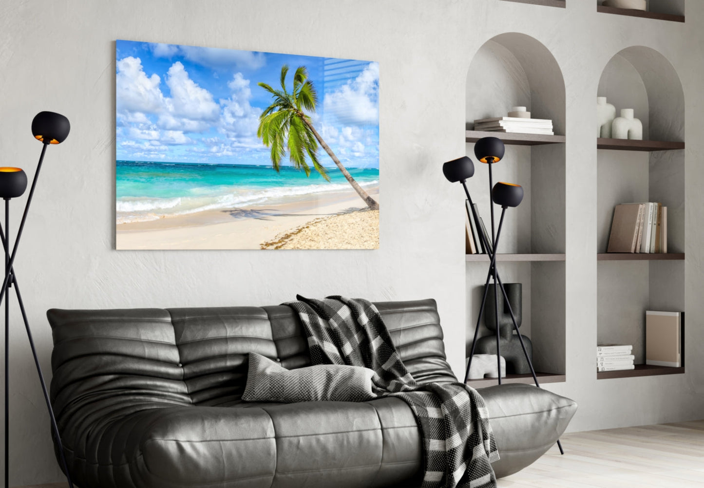 Beach scene glass wall art with palm tree and turquoise ocean displayed above black leather sofa in modern living room.