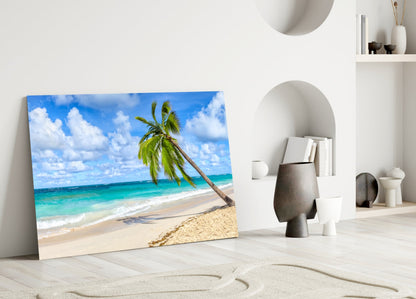 Beach scene glass wall art leaning against white wall in minimalist interior with palm tree and turquoise ocean.