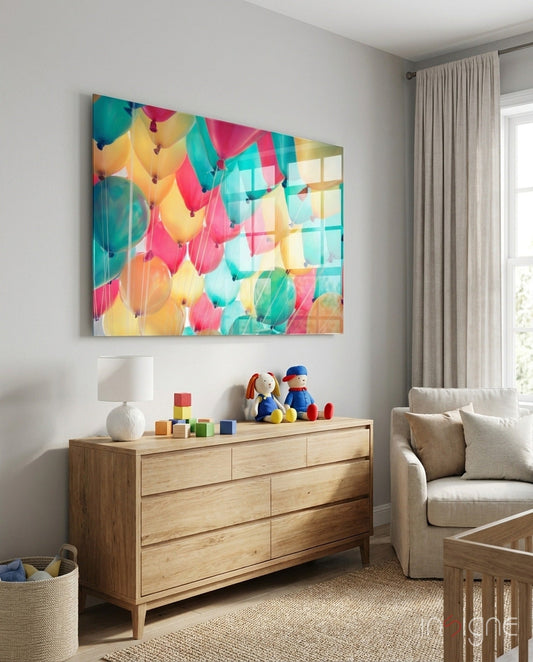 Colorful pastel balloon glass wall art hanging above wooden dresser in neutral nursery room with beige sofa and natural light.