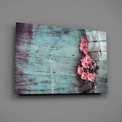 Angled view of glass wall art displaying distressed turquoise wood texture with pink flowers climbing the right edge.