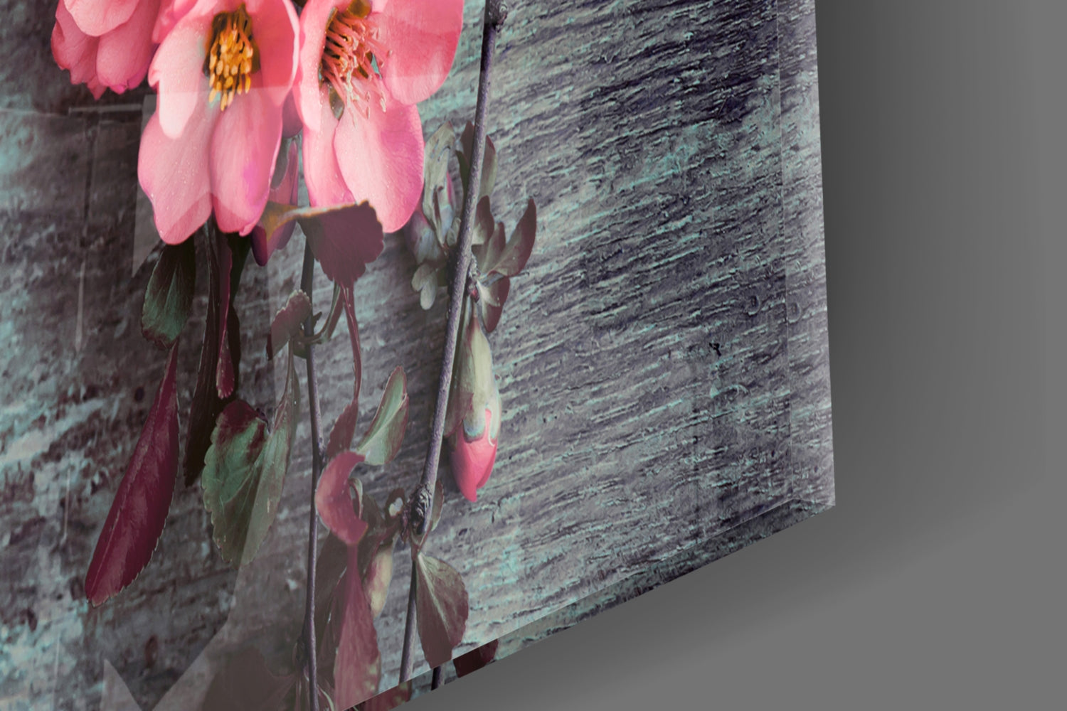 Three-dimensional angled view of glass wall art displaying pink flowers with yellow stamens against weathered teal wooden texture background.