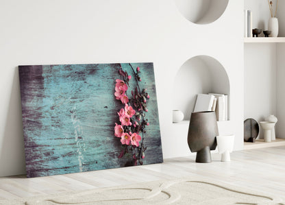 Turquoise weathered wood glass art with pink climbing flowers leaning against white interior wall beside decorative vessels.