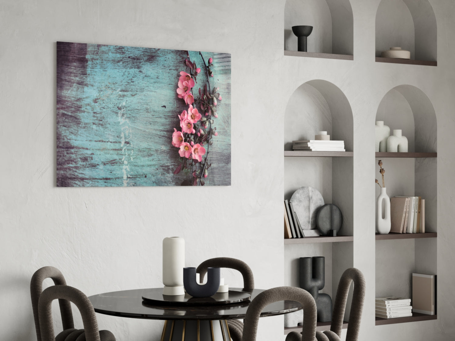 Glass wall art depicting pink flowers on distressed turquoise wood background, displayed above black dining table with chairs.