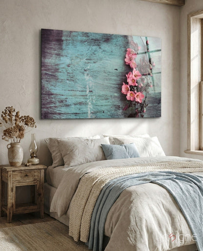 Turquoise distressed wood texture glass wall art with pink flowers hanging on vine, displayed above bedroom bed with neutral linens.