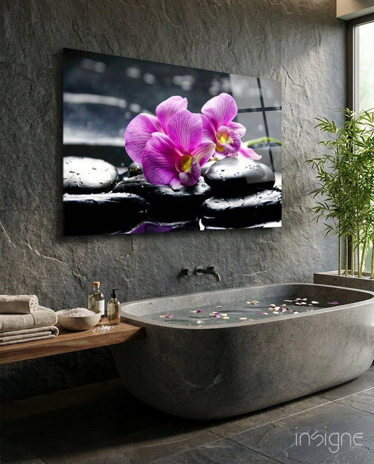 Magenta orchid glass wall art displayed above a concrete bathtub in a modern spa bathroom with gray stone walls.
