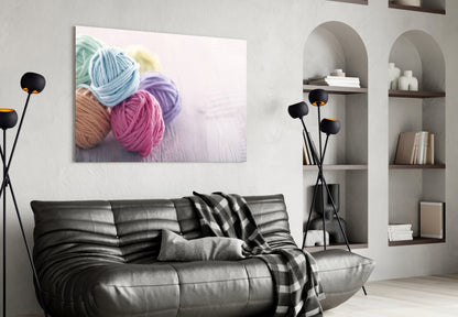 Colorful yarn balls in blue, pink, and brown displayed as glass wall art above a black leather sofa in a modern living room.