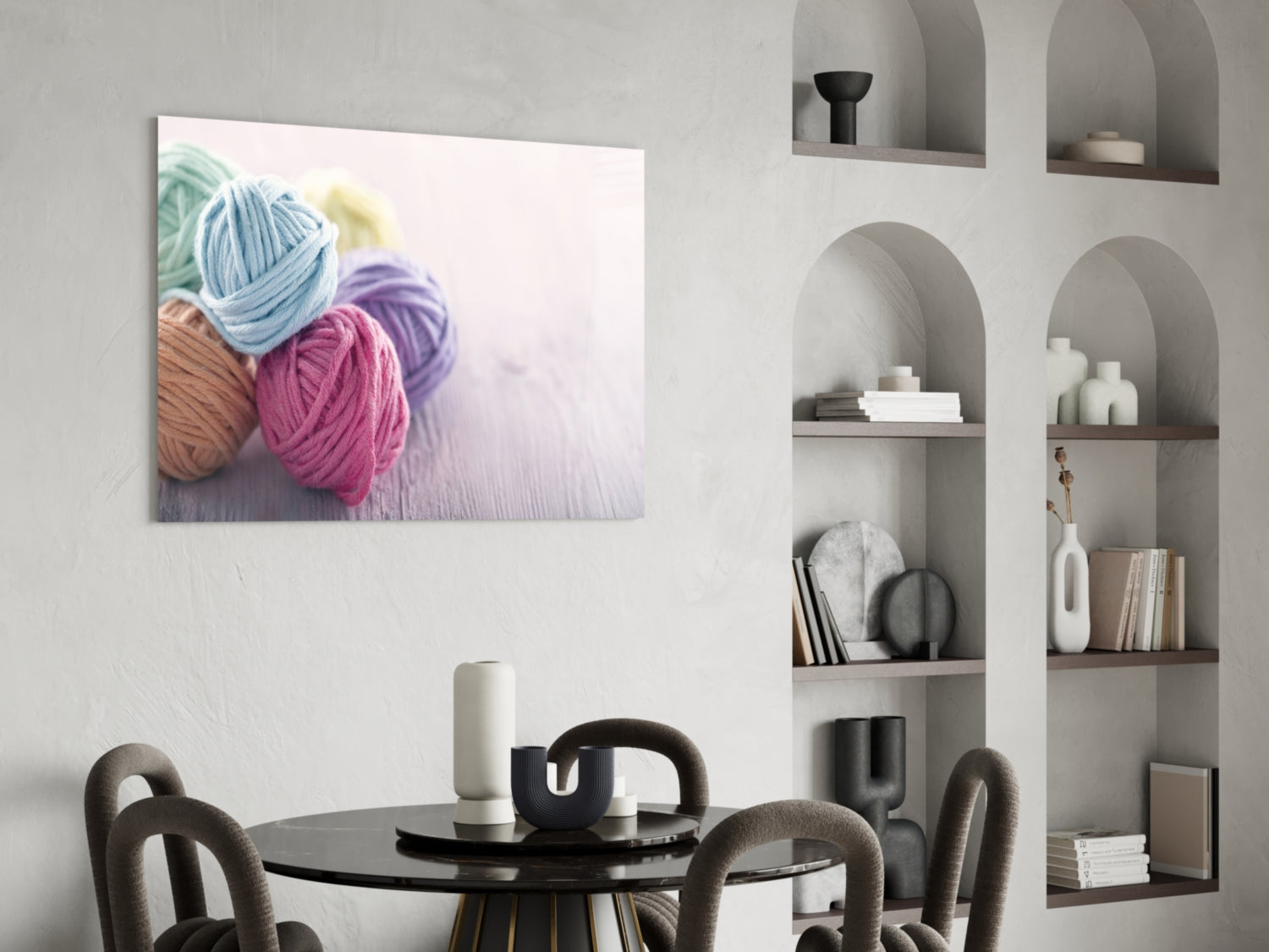Colorful yarn balls in blue, pink, and purple displayed on canvas hanging above a black round dining table with chairs.