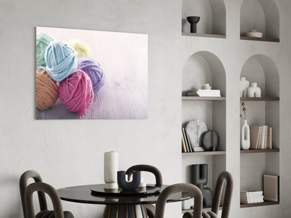 Colorful yarn balls in blue, pink, and purple displayed on canvas hanging above a black round dining table with chairs.