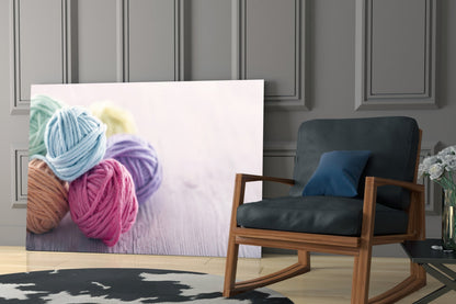 Colorful yarn balls in blue, pink, purple, and green displayed on glass wall art in a modern living room setting.