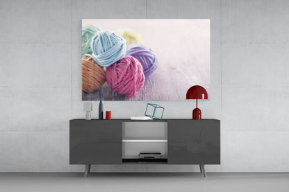 Colorful yarn balls in blue, pink, purple, tan, green, and yellow displayed on a dark console table beneath a mounted glass art print.