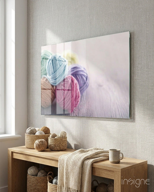 Glass wall art displaying colorful balls of yarn in blue, pink, and purple tones displayed above wooden shelving with baskets.