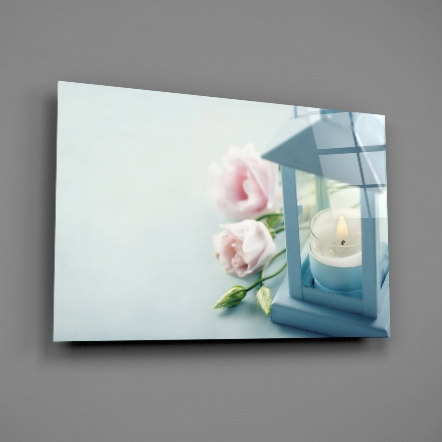 Horizontal glass wall art displaying pink roses and a white candle in blue lantern against light background.