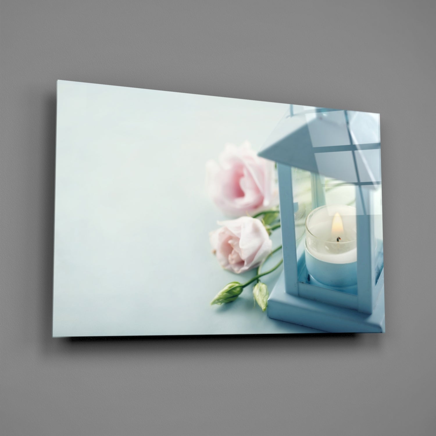 Horizontal glass wall art displaying pink roses and a white candle in blue lantern against light background.