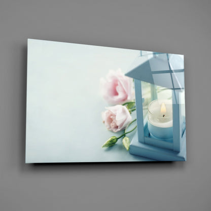 Horizontal glass wall art displaying pink roses and a white candle in blue lantern against light background.