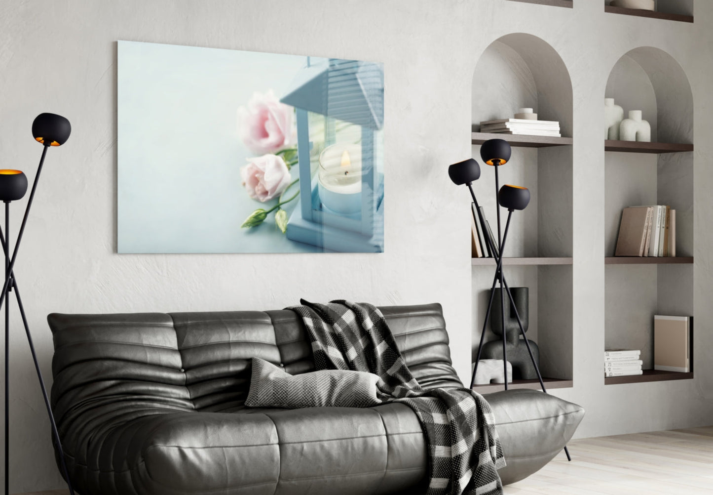 Horizontal glass wall art depicting pink roses and blue lantern with candle, displayed above black leather sofa in modern living room.