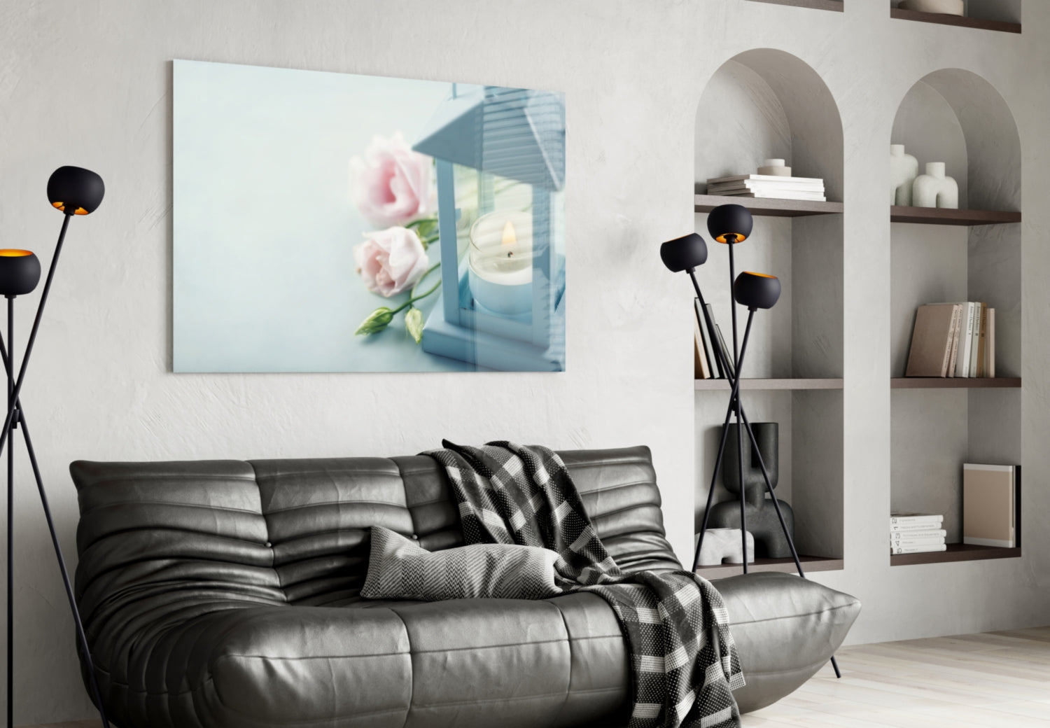 Horizontal glass wall art depicting pink roses and blue lantern with candle, displayed above black leather sofa in modern living room.