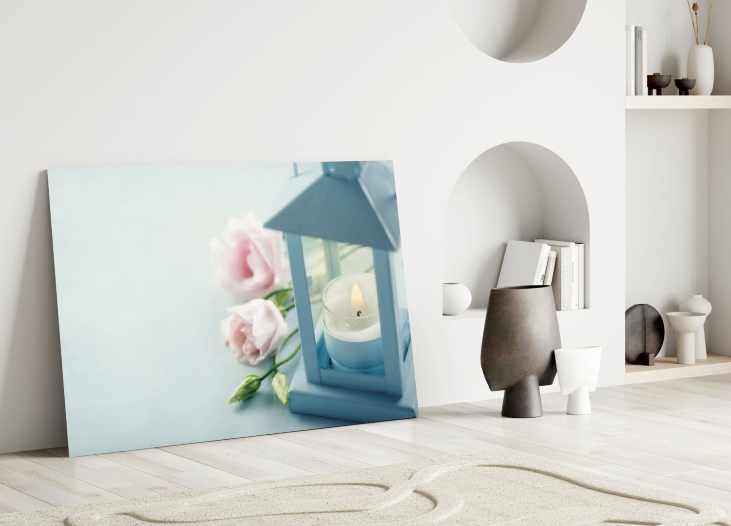 Light blue glass canvas leaning against white wall displays pink roses and blue lantern with candle beside minimalist home décor objects.