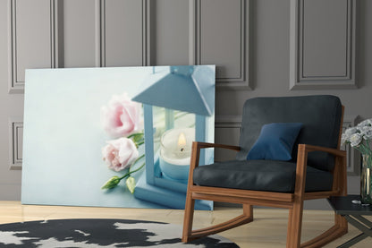 Blue glass wall art displaying pink roses and lit candle in lantern, displayed in modern room setting with wooden chair.