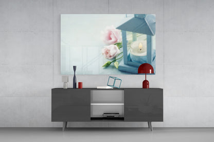 Glass wall art with pink roses and blue lantern with candle displayed above dark media console in modern living room.