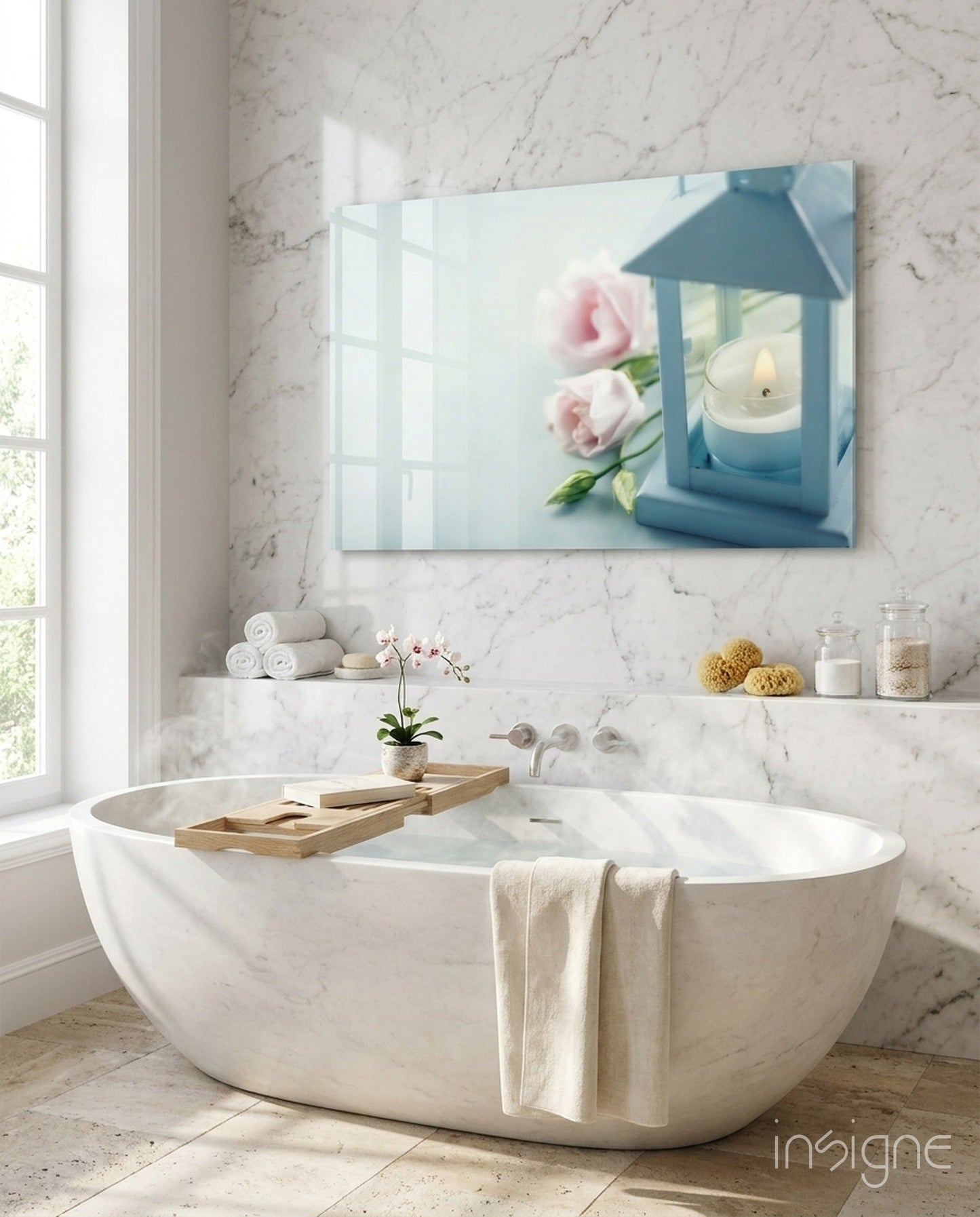 Glass wall art with blue lantern, pink roses, and lit candle displayed above marble bathtub in spa bathroom.