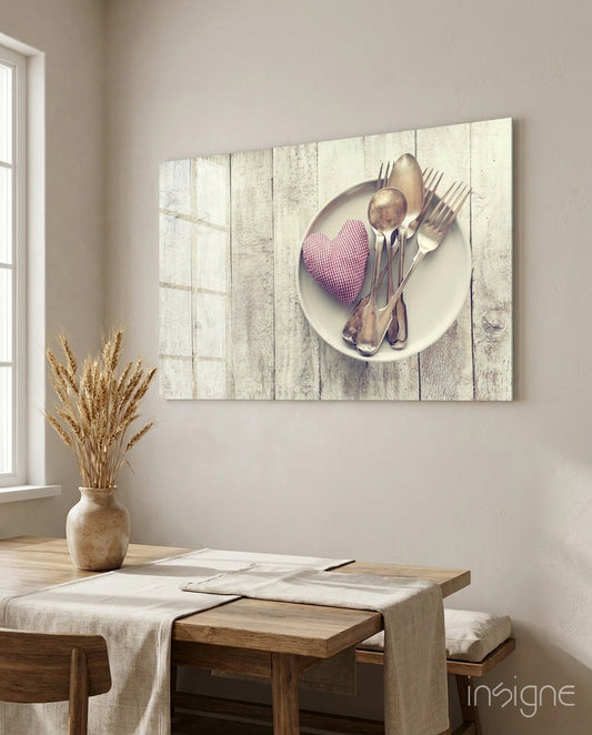 Rustic wooden dining room with glass wall art displaying white plate, cutlery, and pink checkered heart on weathered wood backdrop above table.