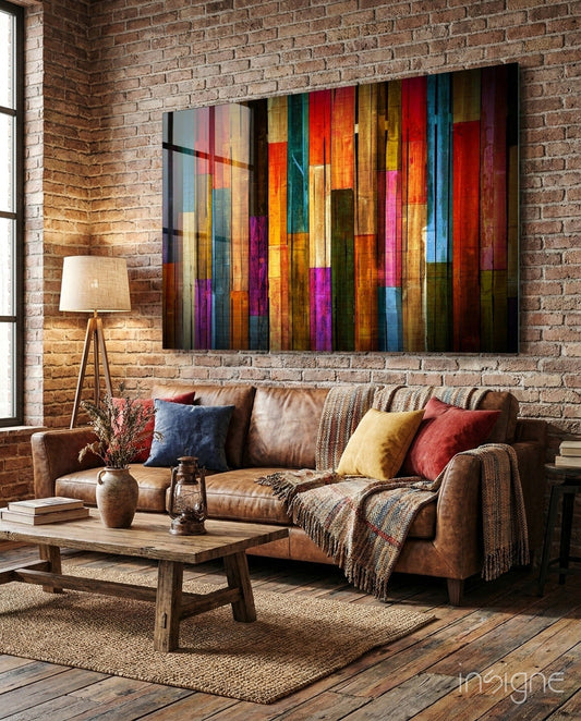 Vibrant multicolor glass wall art with vertical wood plank stripes in reds, oranges, yellows, blues, and purples displayed above a brown leather sofa in a loft interior.