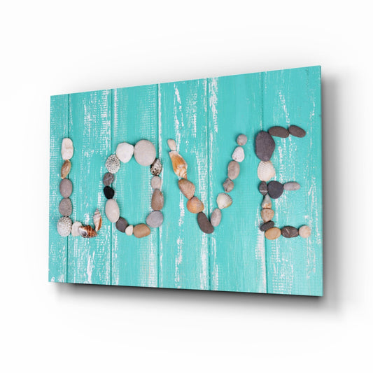 Angled perspective view of turquoise distressed wood panel with pebbles and shells arranged to spell "LOVE" in four vertical columns.