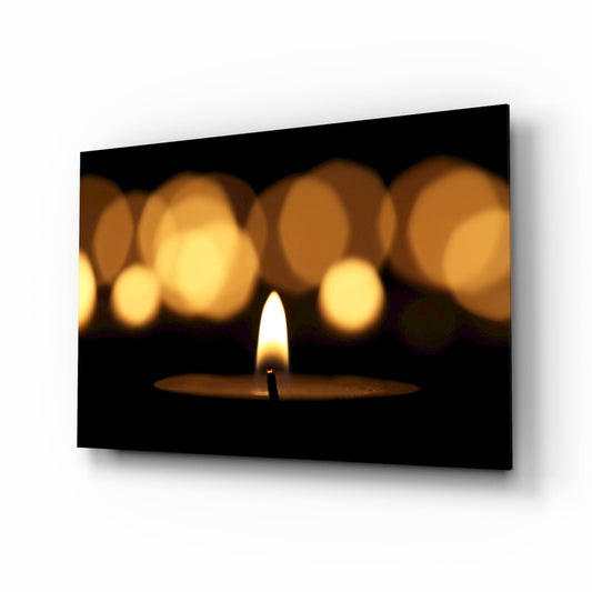 A single lit candle in sharp focus against blurred golden bokeh lights on a black background, displayed as a framed glass wall art piece.