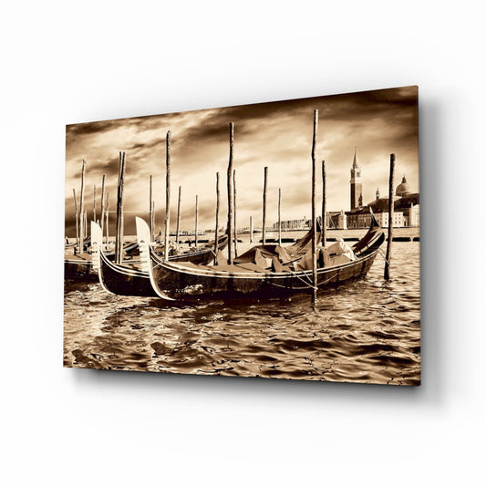 Sepia-toned glass wall art displaying moored gondolas with wooden poles in Venetian waterway, historic architecture visible in background.