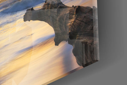 Angled view of glass wall art featuring a dark rock formation archway with golden desert landscape and blue sky visible through the opening.