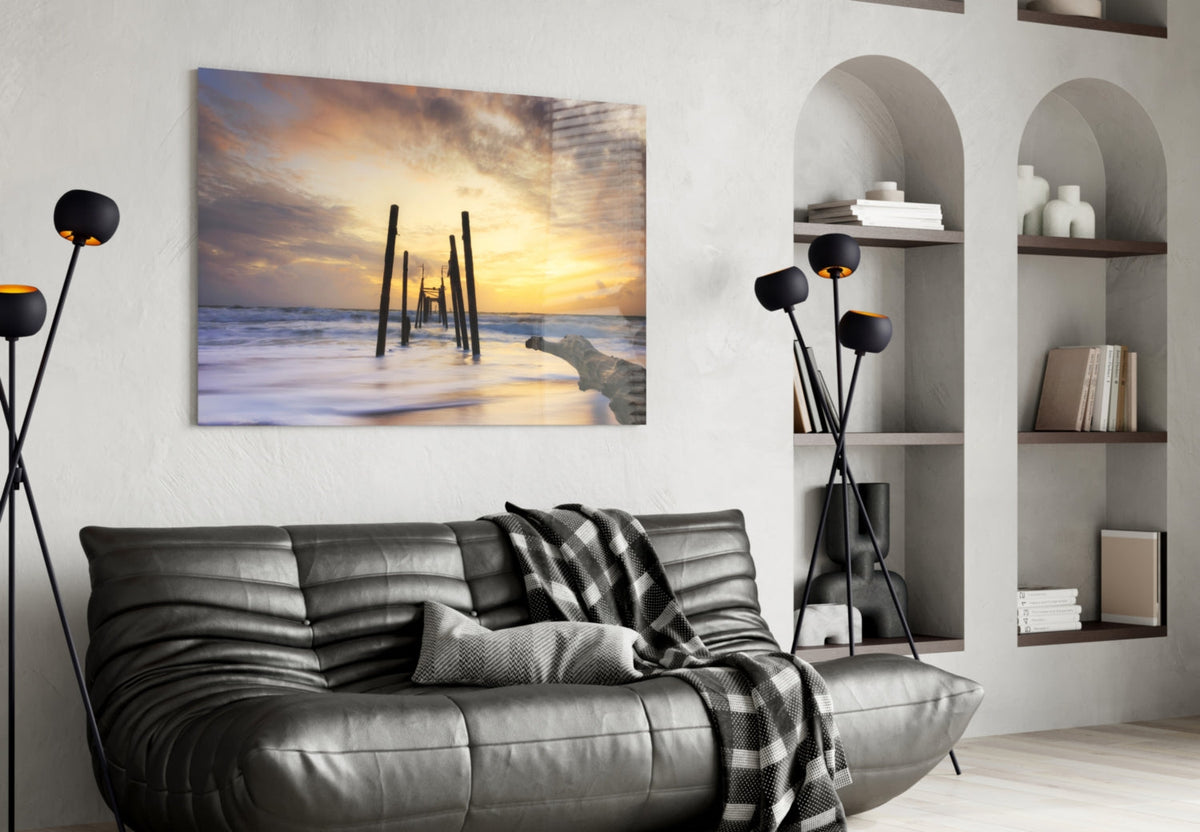 Sunset beach pier glass wall art hanging above gray leather sofa in modern living room interior.