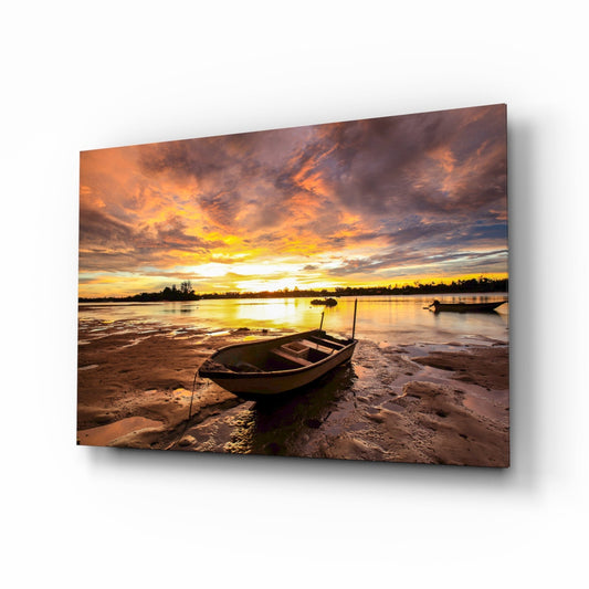 Wooden fishing boat beached at sunset on sandy shore with golden sky and calm water reflected on glass panel.
