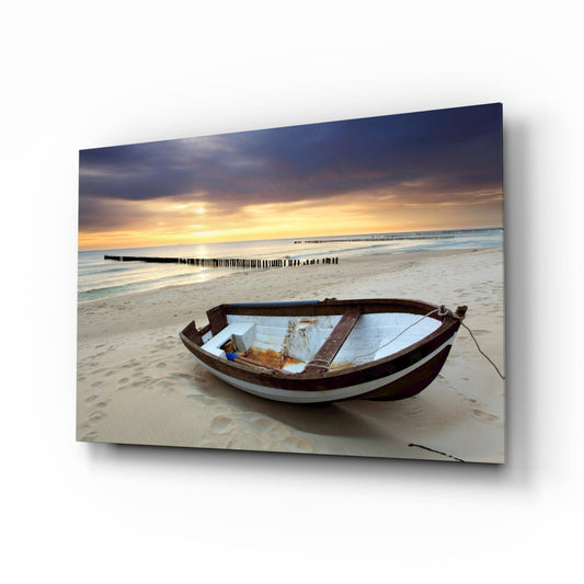 Wooden rowboat with white and brown hull beached on sand at sunset with golden sky and distant pier.