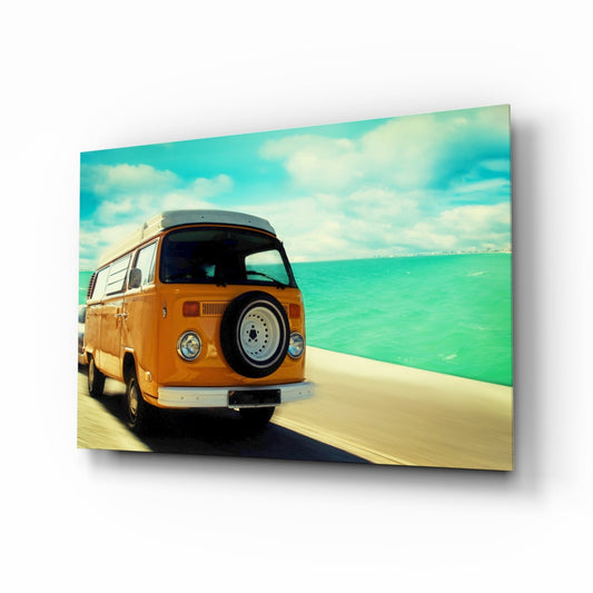 Orange Volkswagen camper van parked on sandy beach facing turquoise sea under blue sky with white clouds, rear three-quarter view on glass panel.