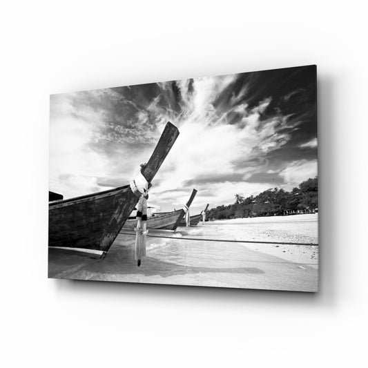 Black and white photograph of weathered wooden fishing boats beached on sand with dramatic cloudy sky and tropical treeline in background.