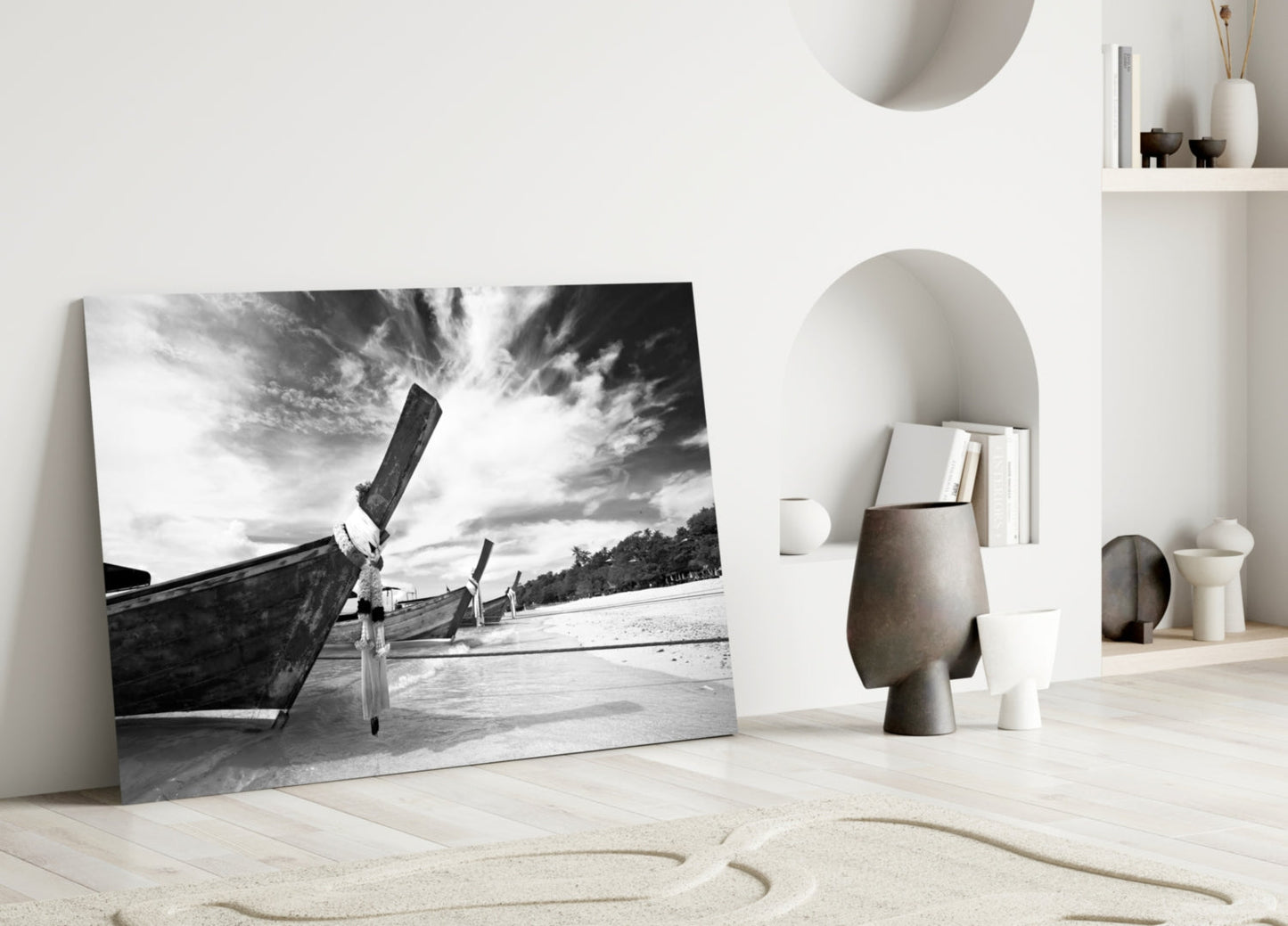 Black and white glass wall art leaning against white wall displaying traditional boats on beach with dramatic sky.