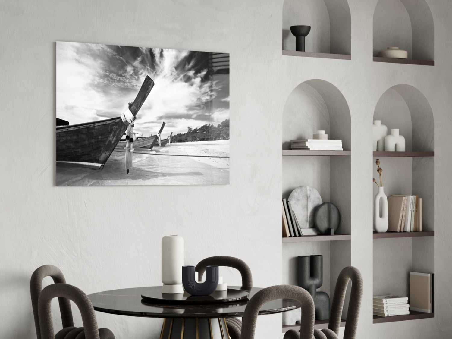 Black and white photograph of wooden boats on a beach with sky, displayed as glass wall art above a round dining table with chairs.