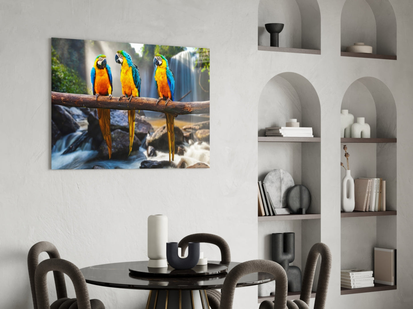 Three blue and gold macaws perched on a branch above a waterfall, displayed as glass wall art in a modern dining room.